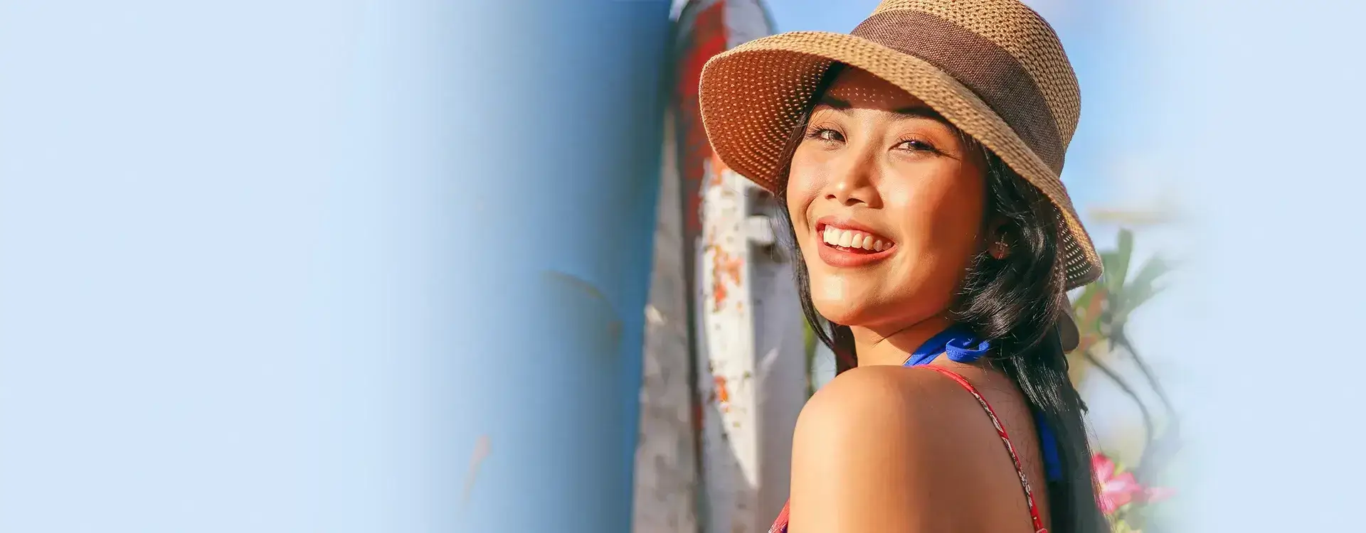 Asian woman smiling in a sun hat with a clear blue sky in the background.