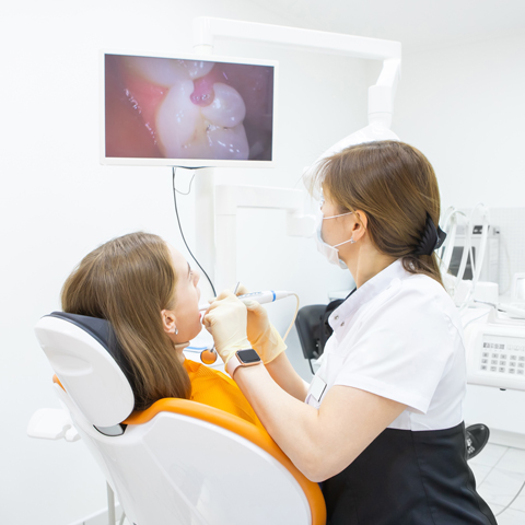 Dentist conducting a detailed oral examination on a patient with real-time intraoral camera feed displayed on monitor.